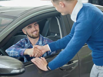 Eine Person in einem blauen Pullover schüttelt die Hand eines Fahrers, der im Auto sitzt, was auf einen Deal oder eine Vereinbarung bei Autoankauf Rheine hinweist.